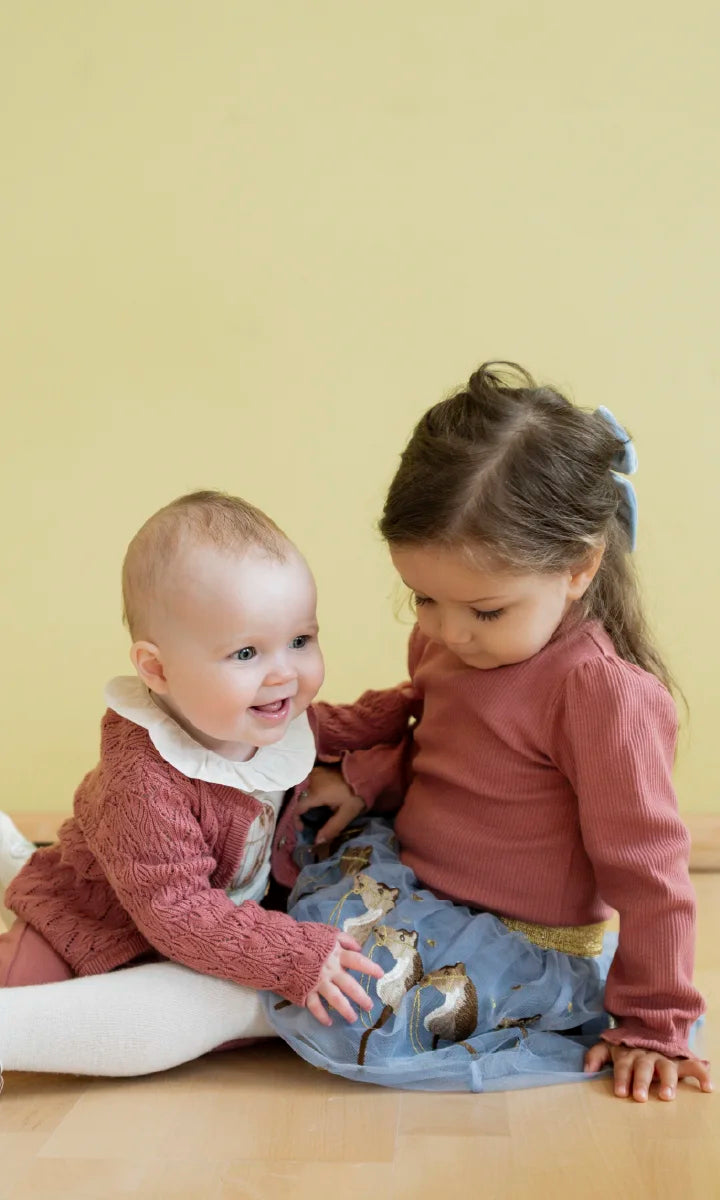 Two children in festive outfits sitting in a red sleigh holding a gift box.